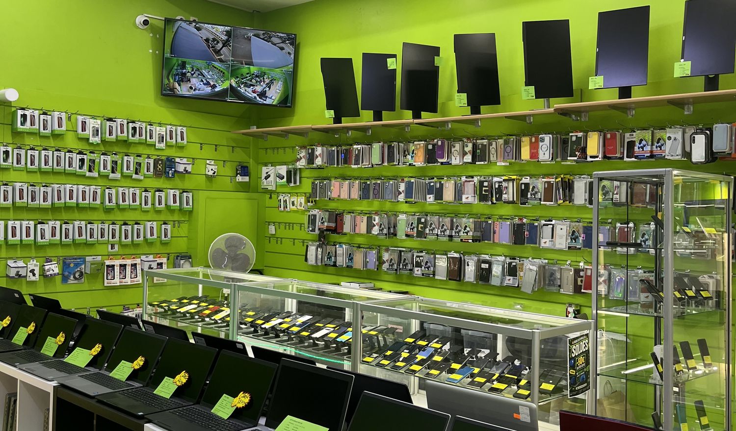 Intérieur du magasin Belgium IT Green : mur d'accessoires, vitrines de smartphones et ordinateurs portables
